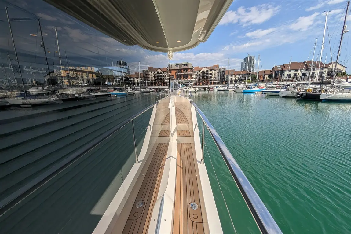 View from a yacht's bow, showcasing the marina, moored boats, and waterfront buildings under a clear blue sky.